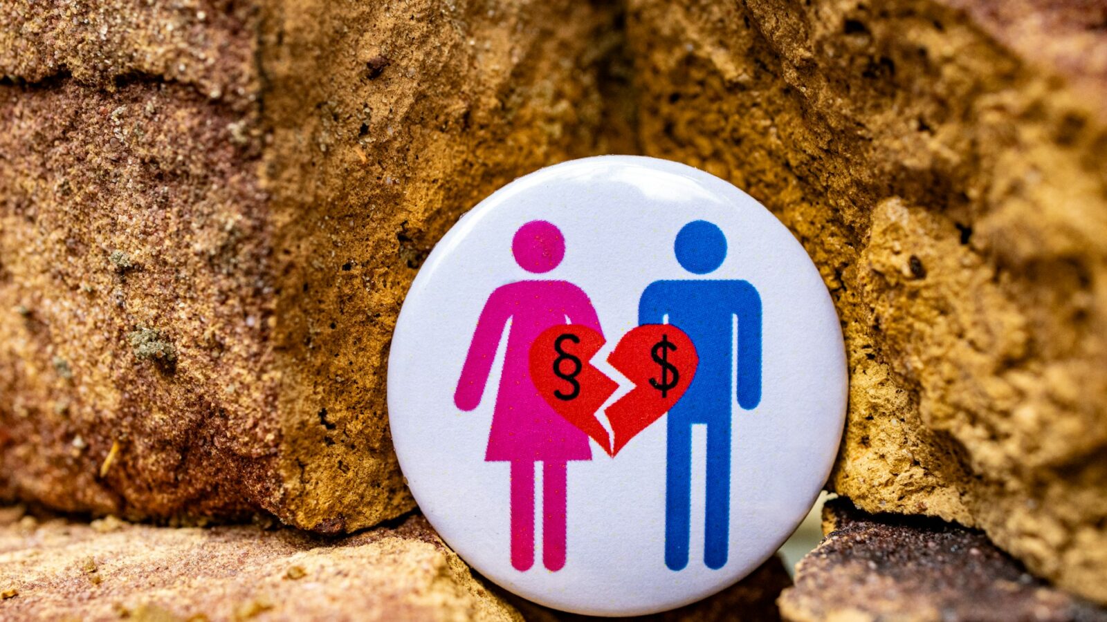 A button with pink and blue stick figures and a broken heart with dollar signs on, representing earning capacity.