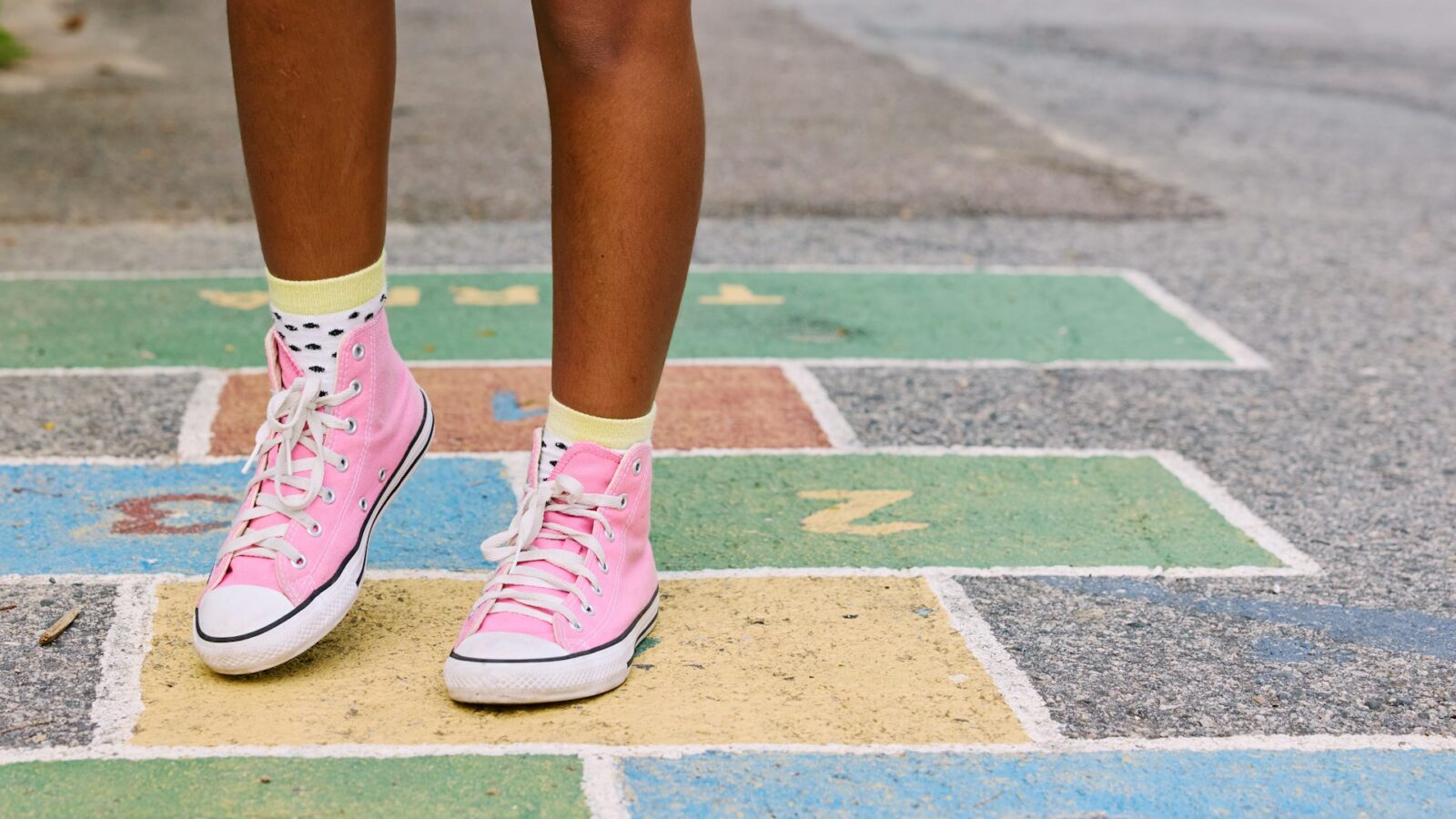 Child's feet in pink sneakers standing on a colorful hopscotch court, illustrating the journey and parenting time modifications children experience.