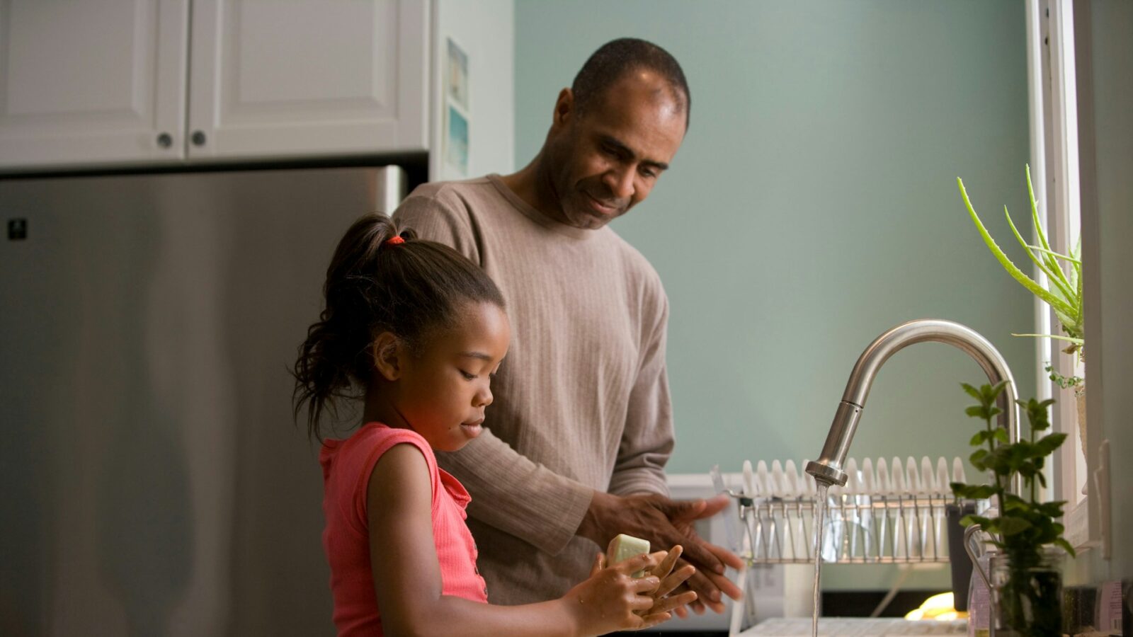 A single father and his daughter are washing their hands together in the kitchen, representing parallel parenting plans after separation and divorce in Ontario.
