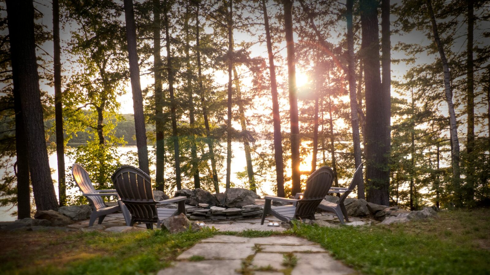 A group of Muskoka chairs around a fire pit on a property overlooking the lake as the sun sets, representing the family cottage during divorce.