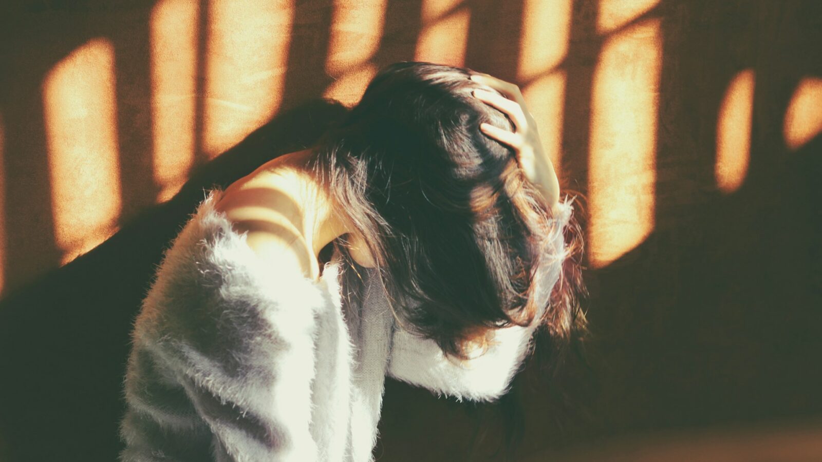 A woman holding her head in her hands, hiding her face, representing the tort of intimate partner violence recognized by the Supreme Court of Canada in Ahluwalia v. Ahluwalia.